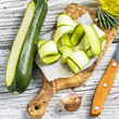 Thin slices of fresh zucchini on the cutting board  the olive tree  a simple wooden table with  bottle   oil for cooking homemade spring afternoon. The concept  home seasonal  natural food.