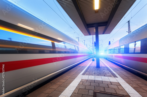 Fotomural Trenes de pasajeros de alta velocidad en la plataforma del ferrocarril en movimiento al anochecer