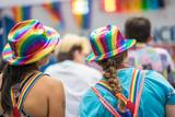Fototapeta Tęcza - Young brunette woman in a crowd celebrating Pride Parade. Wearing colorful rainbow accessories. Soap bubbles floating around her. Supporting marriage equality and LGBT rights.