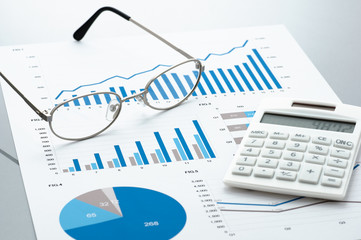 Poster - Business document, glasses, and calculator on gray reflection background.
Many graphs and charts. Concept image of data reviewing.
