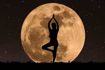 silhouette young woman with good shape practicing yoga under full moon at night with stars