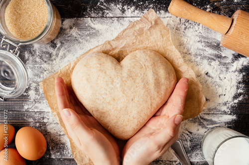 Fotografie, Obraz female hands holding dough in heart shape top view