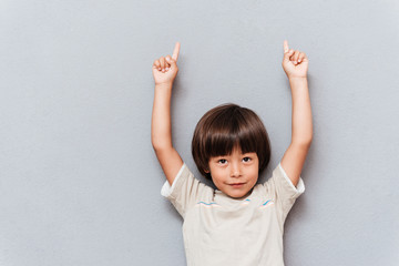 Portrait of happy little boy pointing up with both hands