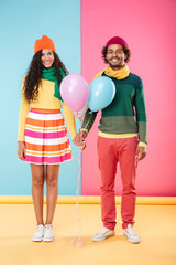 Wall Mural - Happy african young couple in hats and scarves holding balloons