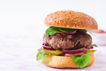 Big sandwich - hamburger burger with beef, pickles, tomato and red onions on a light background.