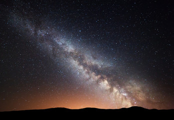 Wall Mural - night landscape with amazing milky way and yellow light at mountains. starry sky with hills at summe