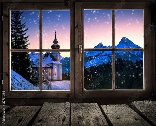 Fototeppich - Blick aus dem Fenster einer Holzhütte auf eine Winterlandschaft mit kleiner Kirche (von Visions-AD)