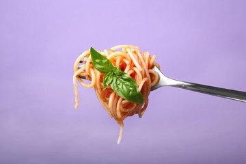 Fork with pasta and basil on color background