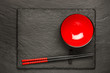 Two chopsticks and red plate on black stone background with copyspace, top view