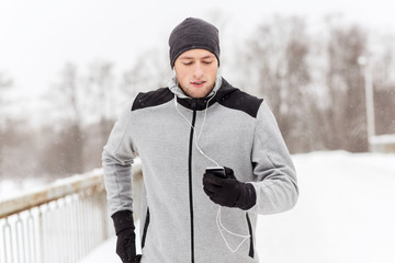 Canvas Print - happy man with earphones and smartphone in winter