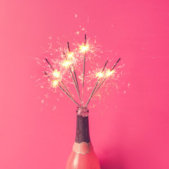 Wall Mural - Champagne bottle with sparklers on pink background. Flat lay.