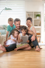 Wall Mural - At home, a family sitting on wooden floor while using a tablet