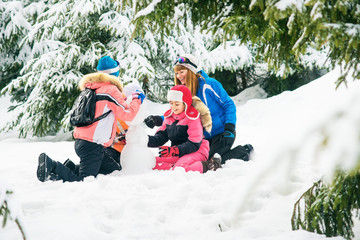 girls playing with snow in the winter forest. Girls in ski suits shape snowman,  girl having fun with snow in winter outdoors. Mother and daughter girl playing in the snow. Happy people in winter
