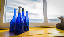 Blue Bottles In A Window Beside The Sea, Newfoundland Canada.
Wide Angle View, Blue Glass Bottles Decorate A Shelf At A Window With A View To The Atlantic In Grand Bank Newfoundland.