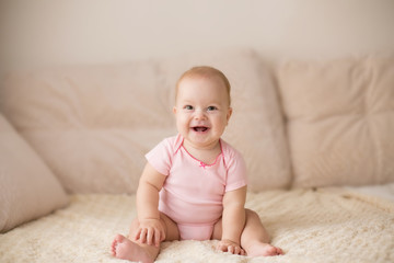 Wall Mural - Cute smiling baby in pink bodysuit on a beige couch...