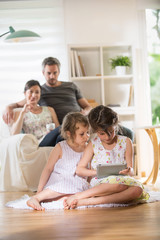 Wall Mural - Cheerful family at home. two sisters play with a digital tablet