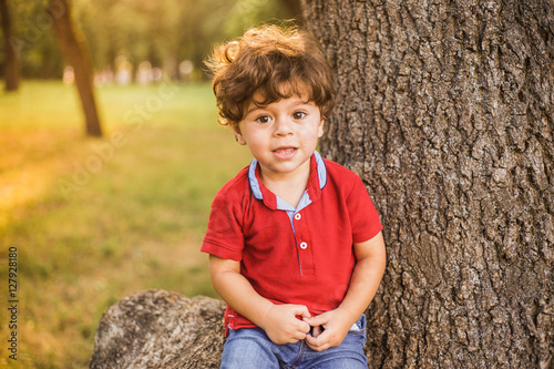 Portrait Of Cute Little Toddler Boy Sitting Under Huge Tree In