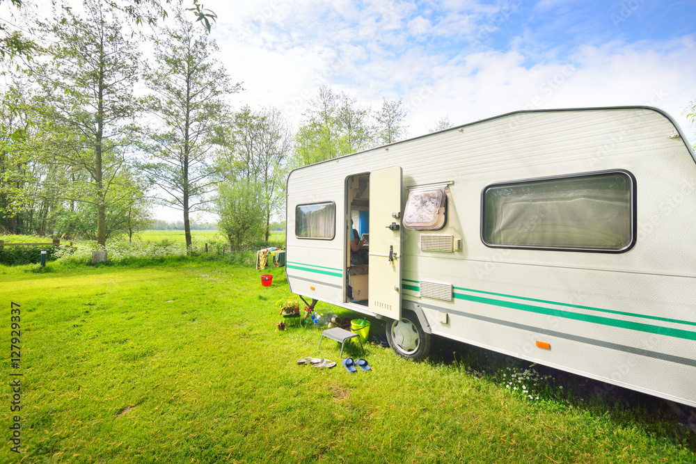 Caravan trailer camping on a green lawn under a tree in springtime - obrazy, fototapety, plakaty 
