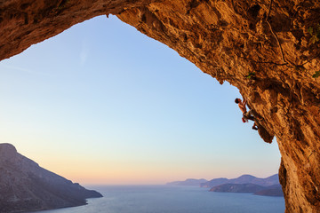 Wall Mural - Young man climbing in cave at sunset