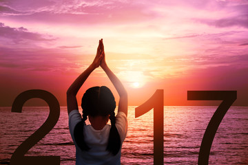 Wall Mural - Happy new year card 2017. Silhouette of girl doing Yoga vrikshasana tree pose on tropical beach with fantastic sunset sky background. Kid standing as part of the Number 2017 sign and watching sunrise.
