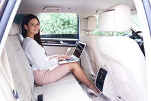 Young Businesswoman With Laptop On Back Seat In Car