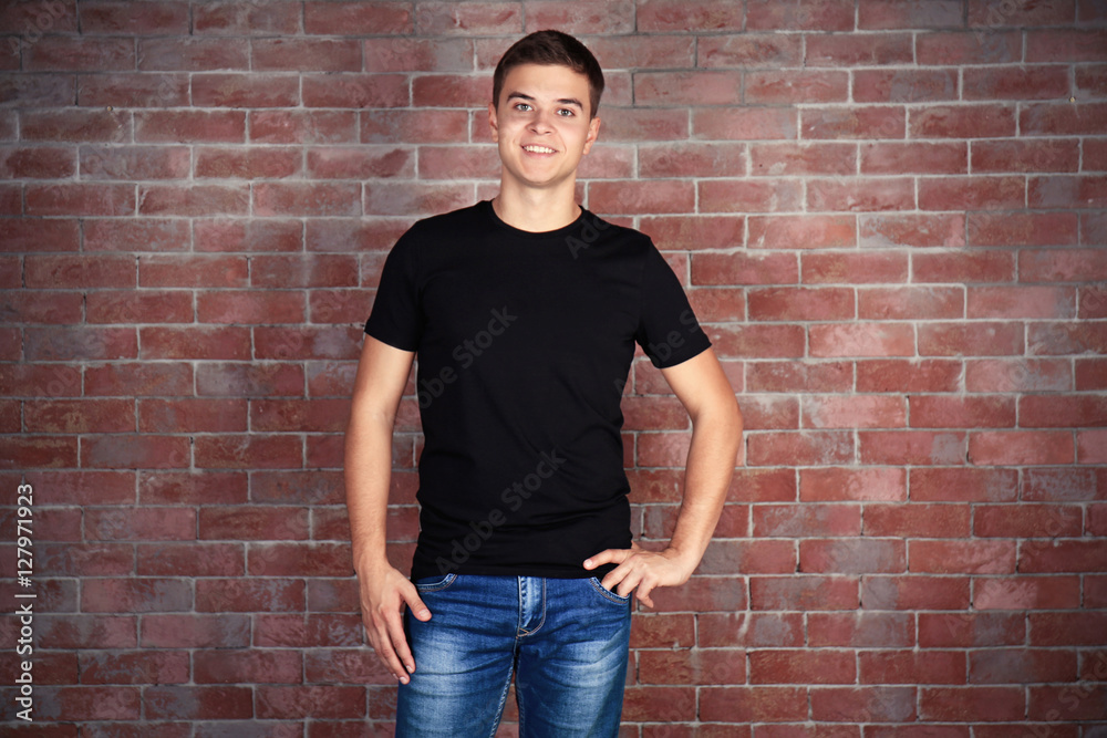 Handsome young man in blank black t-shirt standing against brick wall