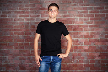 Sticker - Handsome young man in blank black t-shirt standing against brick wall