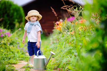 Wall Mural - Toddler boy in straw hat watering plants in the garden