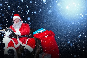 Composite image of santa reading bible with sack of christmas pr