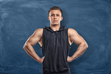 Muscular young man in sportswear standing on the dark blue background.