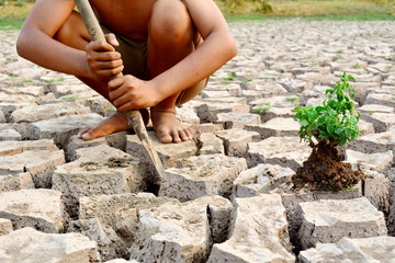 Sad a boy sitting on dry ground .concept drought and hope