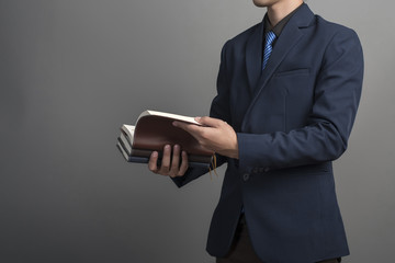 Wall Mural - Close up of businessman in blue suit holding books on gray backg