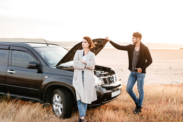 Upset young couple standing near car with open hood