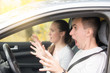 © fizkes - Young scared man driver and a woman passenger put into a dangerous situation, risk of getting into a car accident. Driving instructor and student screaming before crash looking in windshield window