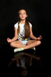 Śliczna dziewczynka medytuje, ćwiczy jogę, na czarnym tle.
