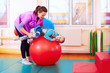 © Olesia Bilkei - cute kid with disability has musculoskeletal therapy by doing exercises in body fixing belts on fit ball