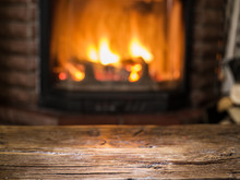Old Wooden Table And Fireplace With Warm Fire On The Background.