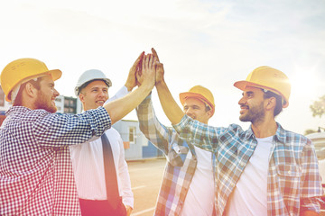 Wall Mural - close up of builders in hardhats making high five