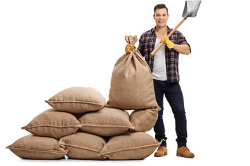 Canvas Print - Young farmer standing next to pile of burlap sacks and holding s