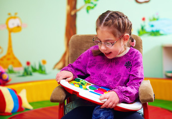 cute girl in wheelchair playing with developing toy in kindergarten for children with special needs