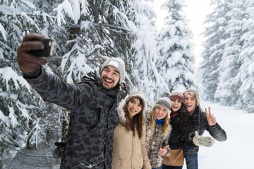 Wall Mural - Man Hold Smart Phone Camera Taking Selfie Photo Friends Smile Snow Forest Young People Group Outdoor Winter Pine Woods