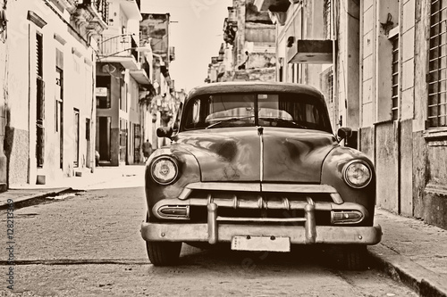 Cuadros en Lienzo Sepia toned vintage classic american car parked in a street of O