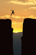 © PThira89 - Man jump through the gap between hill.man jumping over cliff on sunset background,Business concept idea