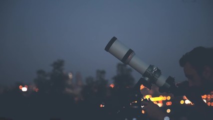 Wall Mural - man looking at the stars with telescope with de-focused city lights.