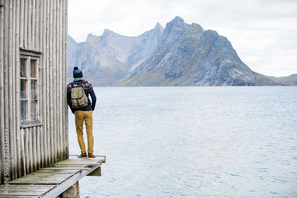 man looking at the mountains, standing on a wooden pier - obrazy, fototapety, plakaty 