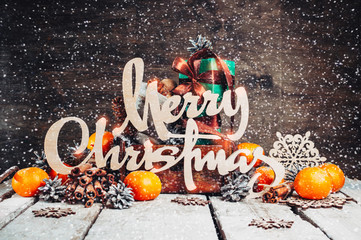 Wall Mural - Christmas home decoration, Wood rustic Xmas background with wooden letters,Cinnamon sticks,Nuts.Ornaments.Gifts in Boxes,Falling snow