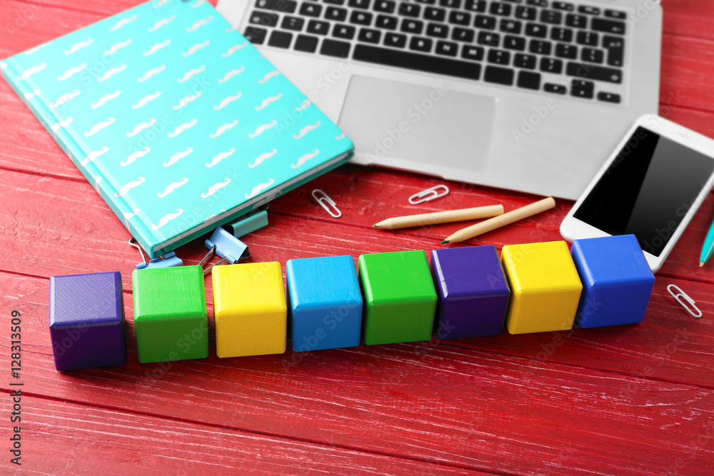 Laptop, copybook and wooden cubes on color background