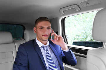 Young businessman sitting in car and talking on phone