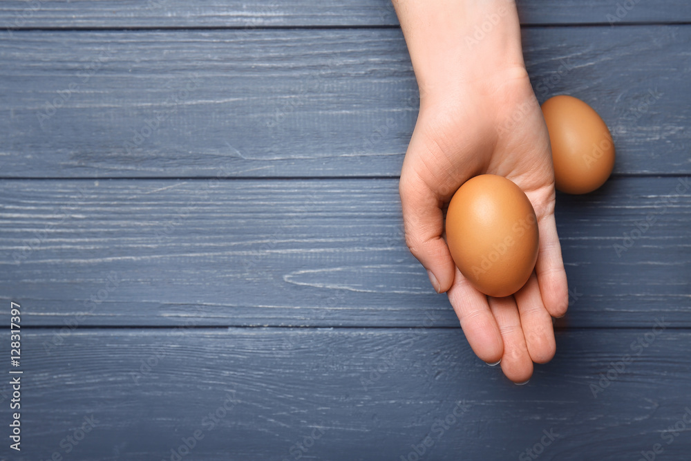 Female hand with egg on wooden background