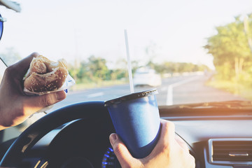 Man is dangerously eating hot dog and cold drink while driving a car